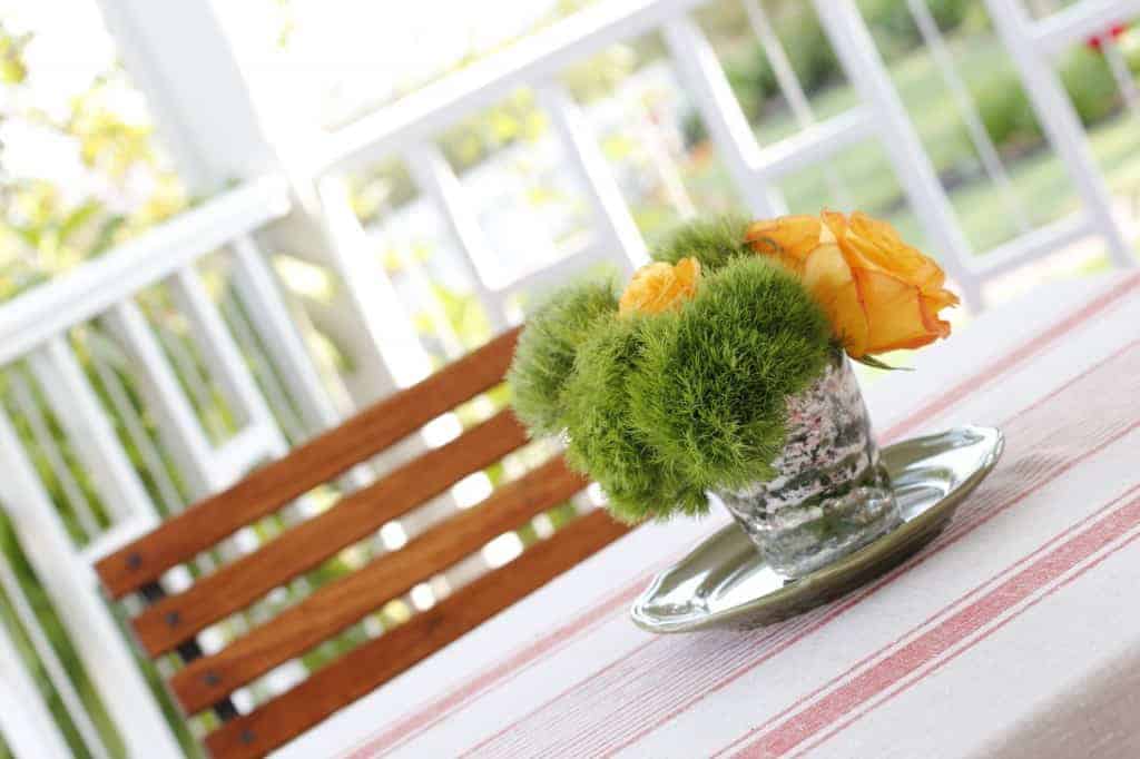 a vase with yellow and green flowers sits on top of an outdoor table