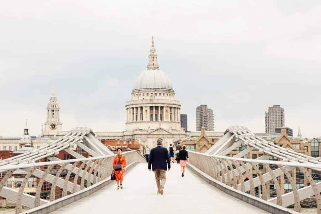 pedestrians walk on a bridge in London with a cathedral in the background