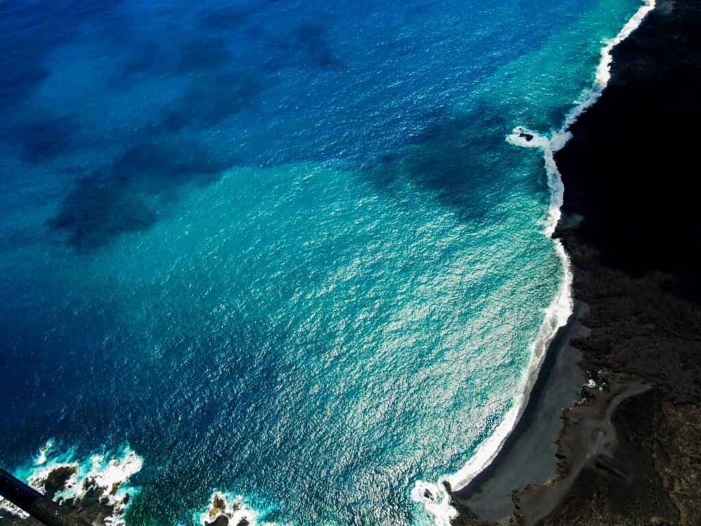 turquoise ocean waves hitting a black sand beach