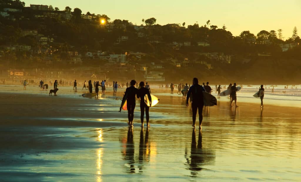 surfers walk on La Jolla shores beach at sunset