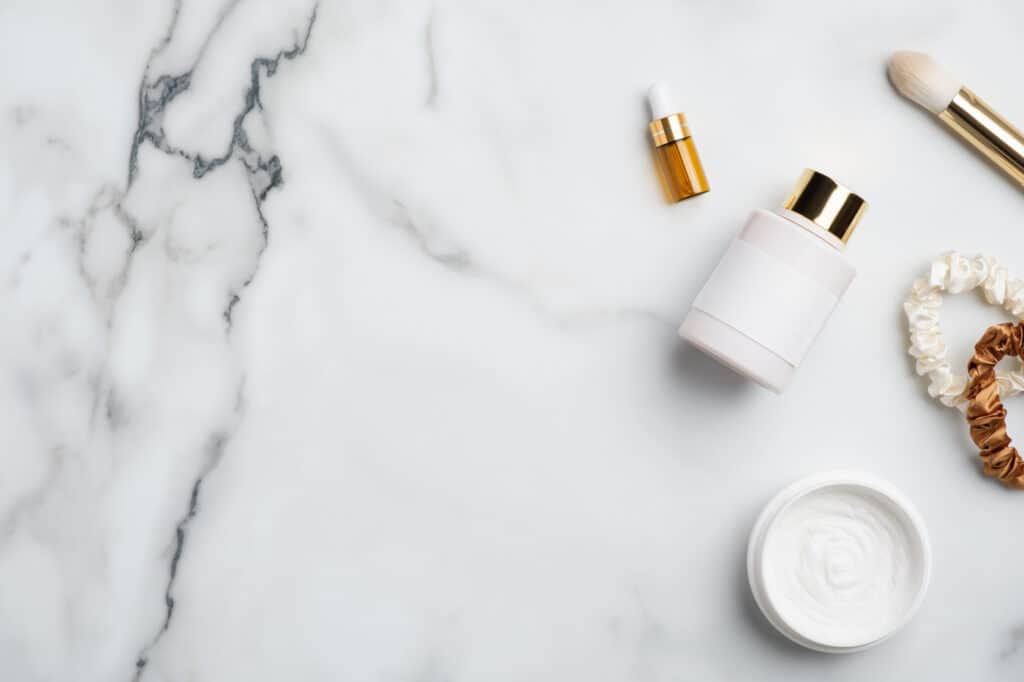 Natural skincare cosmetic products on white marble desk. Flat lay, top view body lotion, serum essential oils, moisturizer cream jar, female accessories.