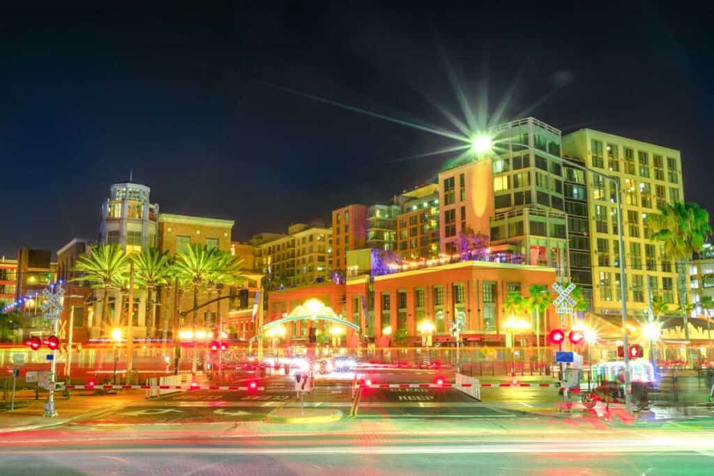 Pedicabs lighting, cars and metro line stop at level crossing in Harbor Drive between Marina district and Gaslamp Quarter in San Diego Downtown, California, USA. Light trails effect by night.