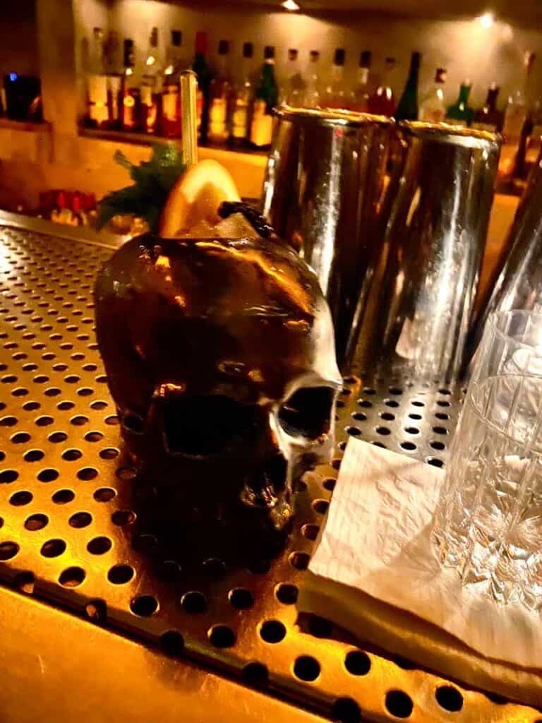 specialty cocktail inside a skull shaped glass sits on a bar