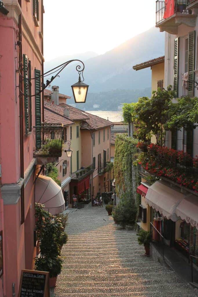 Looking down a cobblestone staircase lined with red and yellow buildings in Bellagio Italy