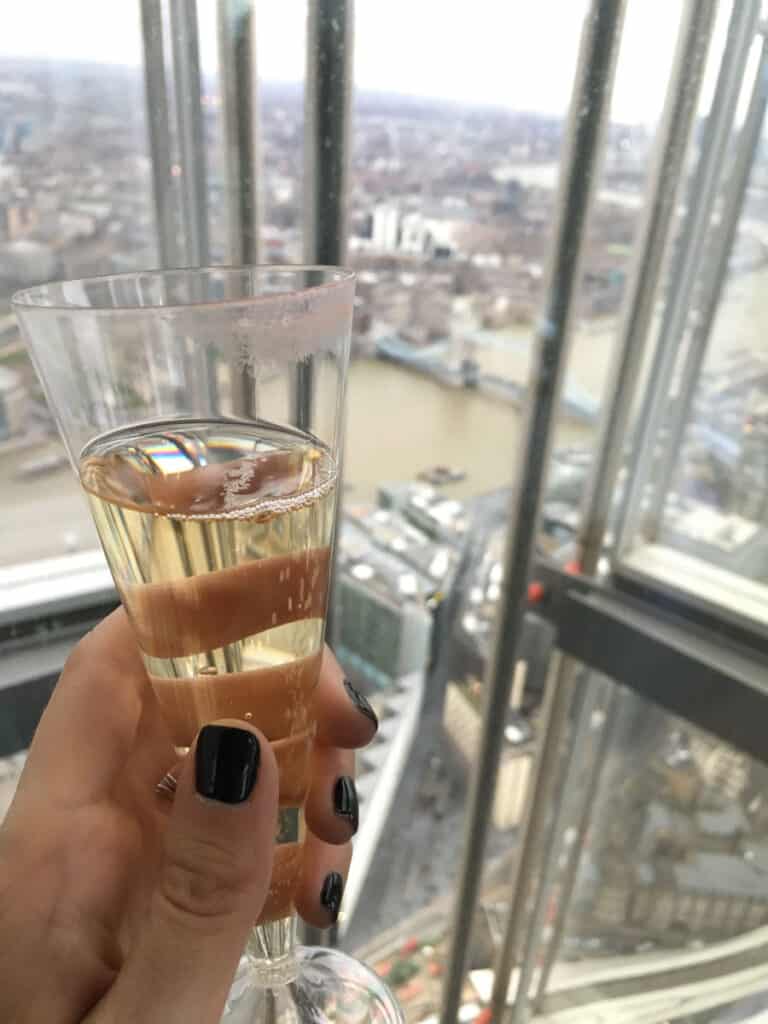 A woman's hand holding a glass of champagne with a view of London in the background