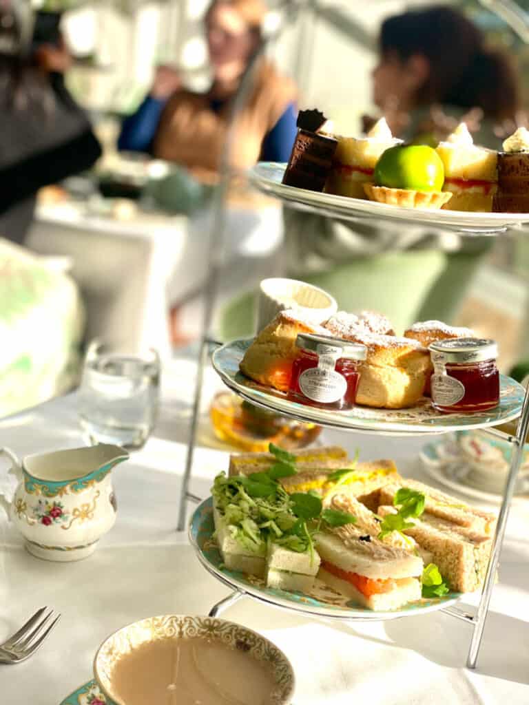A three-tiered serving platter holds sandwiches, scones and desserts