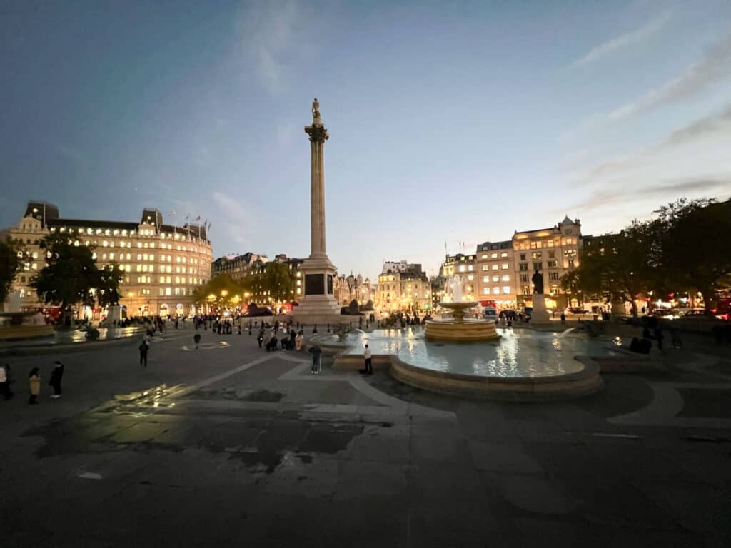 Buildings and a large column lit up in the evening at Trafalgar Square