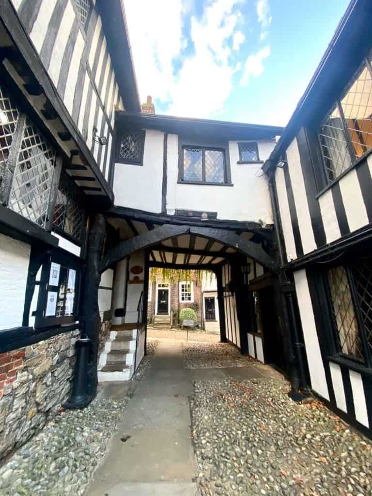 two Tudor style buildings on either side of a cobblestone street are joined by a bridge