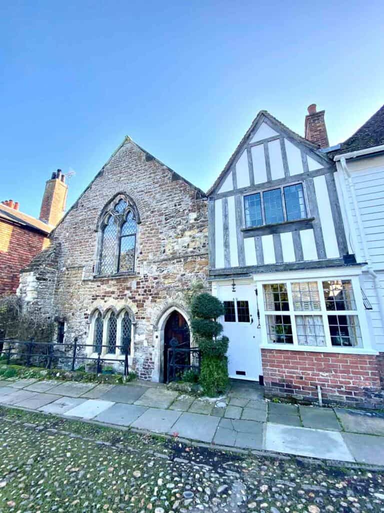 a stone building connects to a tudor style building on a cobblestone street