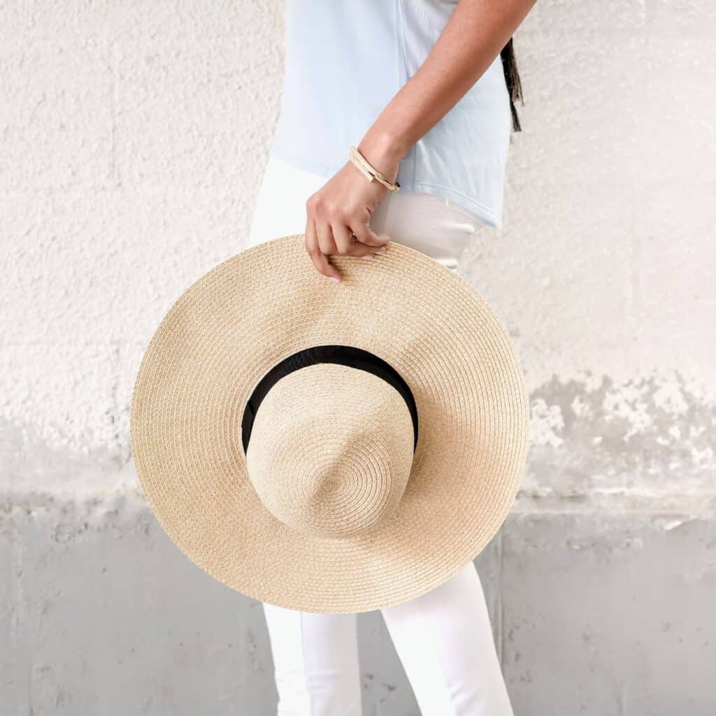 Woman holding sunhat standing against a wall.