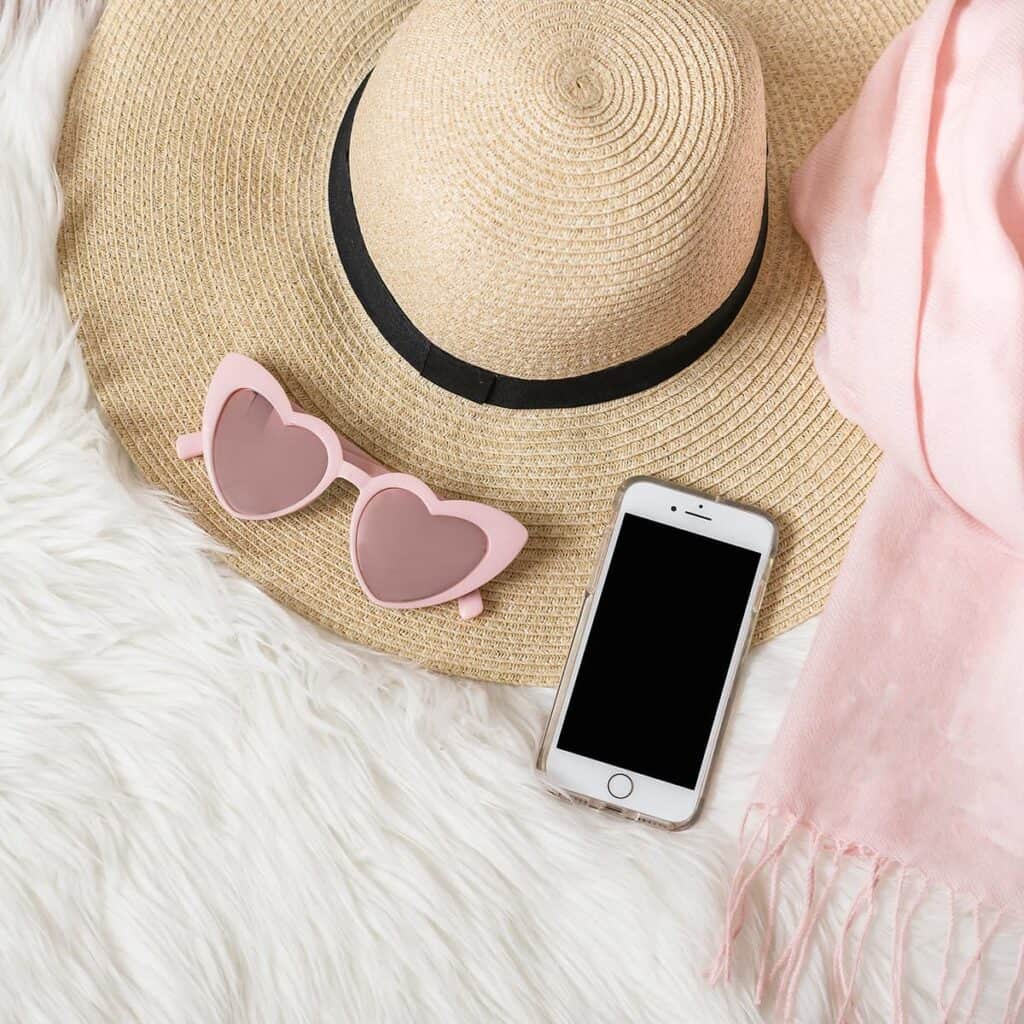 Sunhat, heart glasses and phone sitting on white rug.