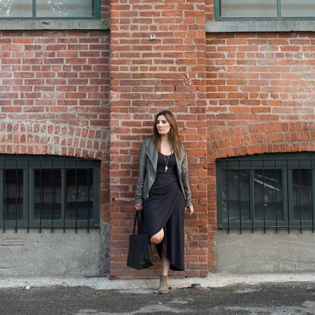 Jessica in a black dress leaning against a brick wall.