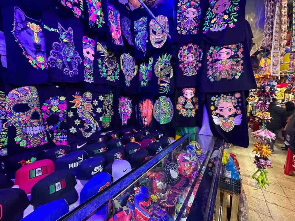 black t shirts with neon artwork hung up for sale at a market in Mexico City