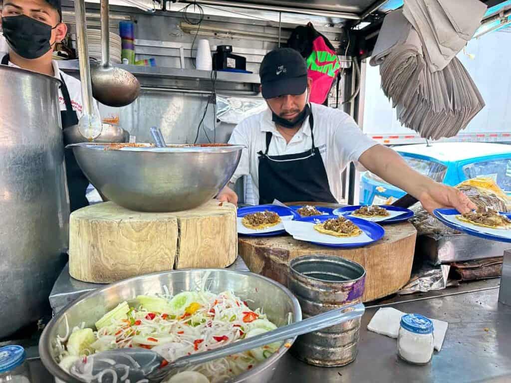 Man behind a steel counter serves street food tacos in Mexico City