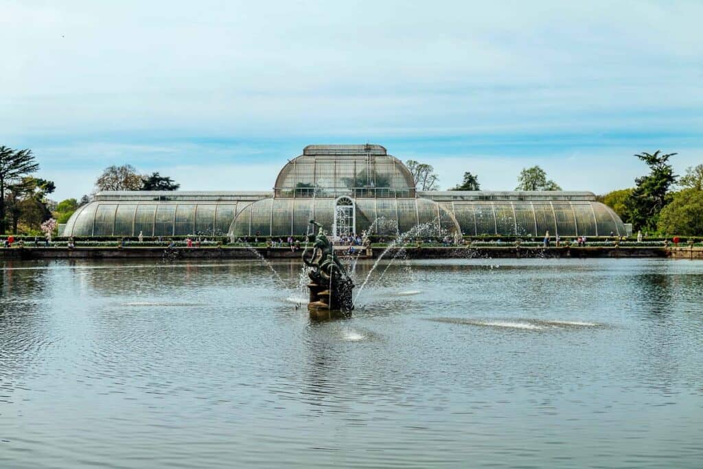 A glass conservatory sits behind a large fountain in KEW GARDENS, London.