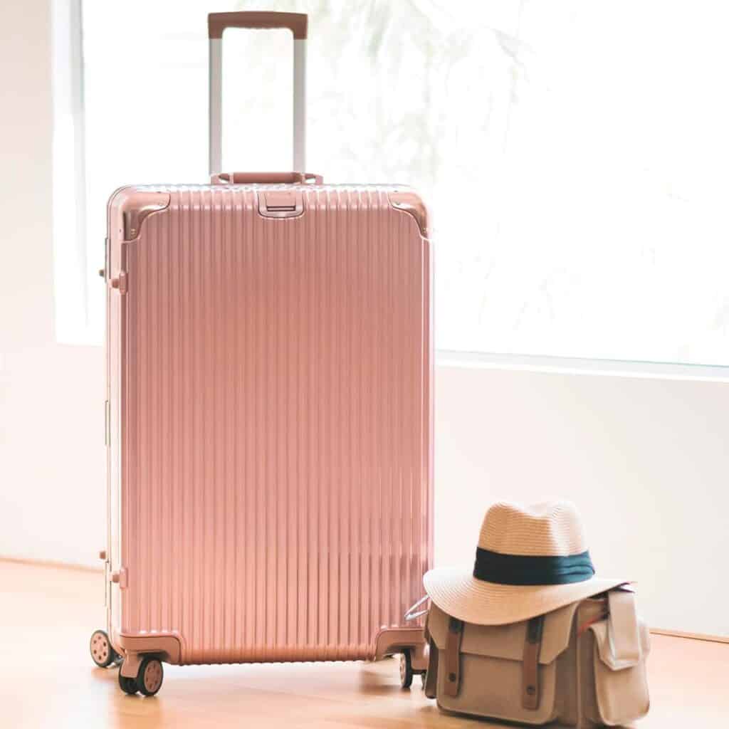 Pink luggage sitting in front of sunny window.