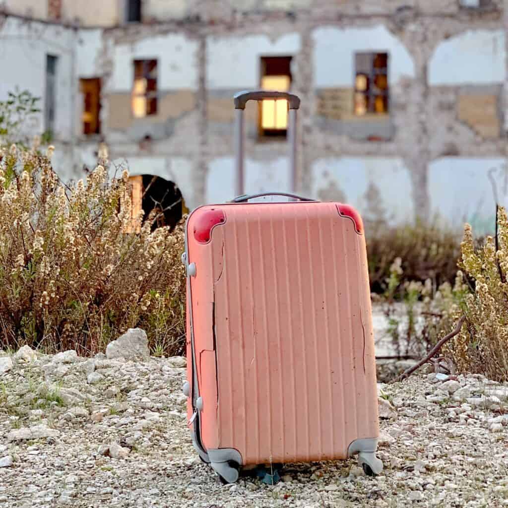 Pink luggage sitting on ground outside.