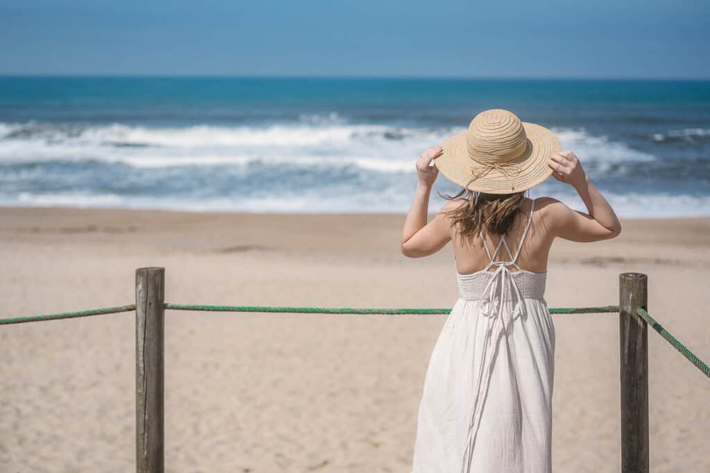 view from the back of a woman at a beach wearing a dress and a sun hat