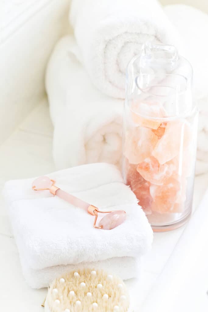 white rolled towels next to a face roller and glass jar of crystals