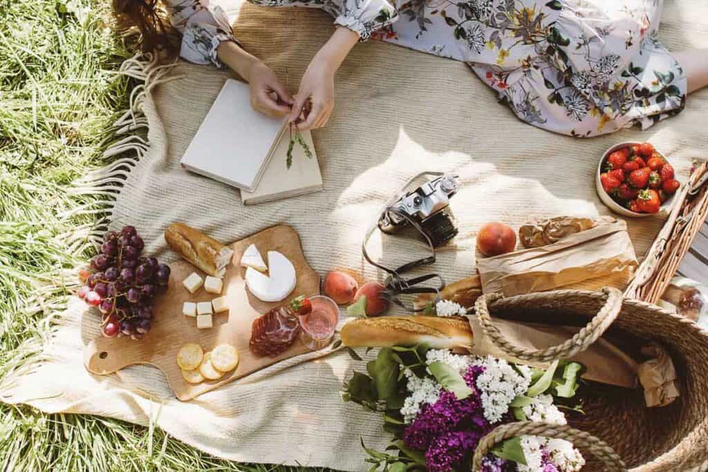 view from above of a picnic basket filled with bread and flowers, and assorted meats and cheeses on a wooden cutting board.