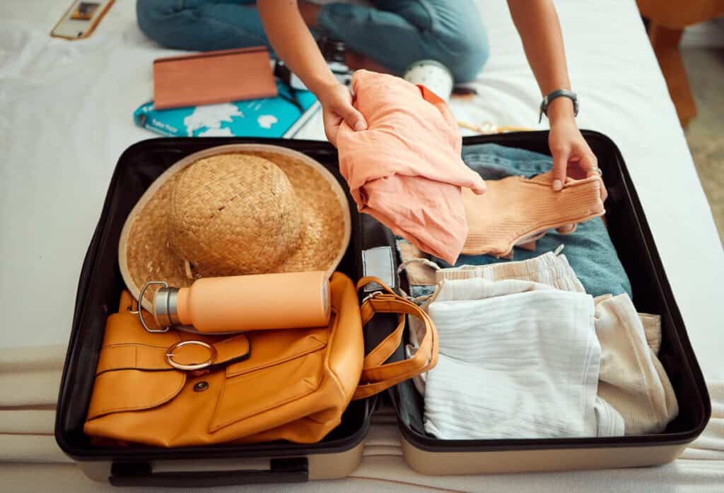 Hands, woman and suitcase on a bed for travel, adventure and summer vacation, packing and clothing. Hand, girl and luggage in a bedroom for travelling, abroad and break, relax and getaway preparation.