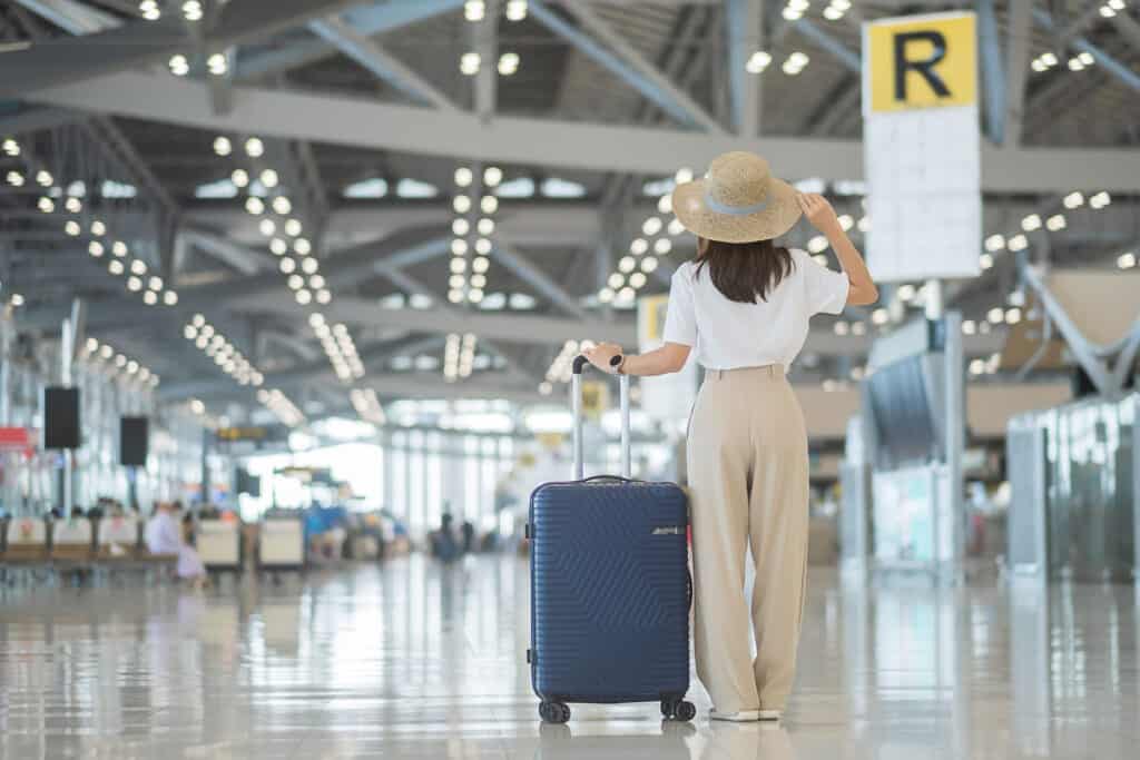 Young woman hand holding luggage handle before checking flight time in airport, Transport, insurance, travel and vacation concepts