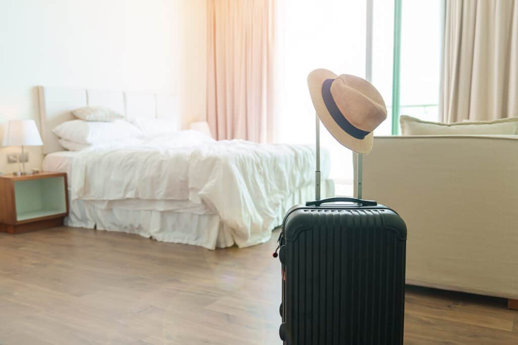Black Luggage with hat in modern hotel room after door opening. Baggage for Time to travel, service, journey, trip, summer holiday and vacation concepts
