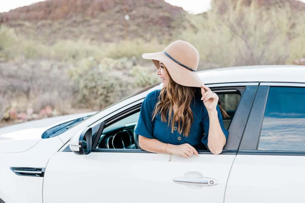 woman wearing a sun hat standing out of a window of a white car